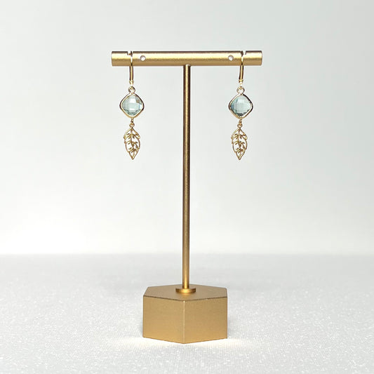 This earring set features a pale green glass charm in a gold bezel with a gold leaf, hung on a French lever back style hook.&nbsp;